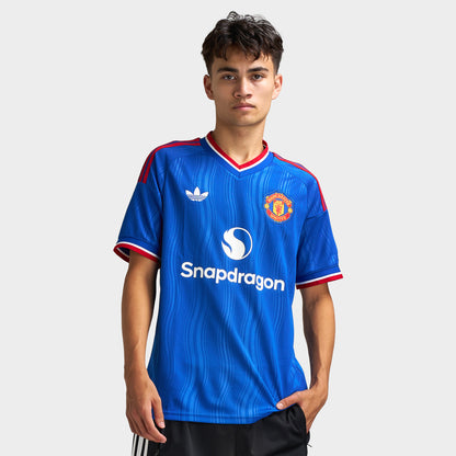 adidas Manchester United Away Jersey. Front view of model wearing team royal blue soccer jersey with red trim, adidas logo, Manchester United crest and Snapdragon sponsor graphic.
