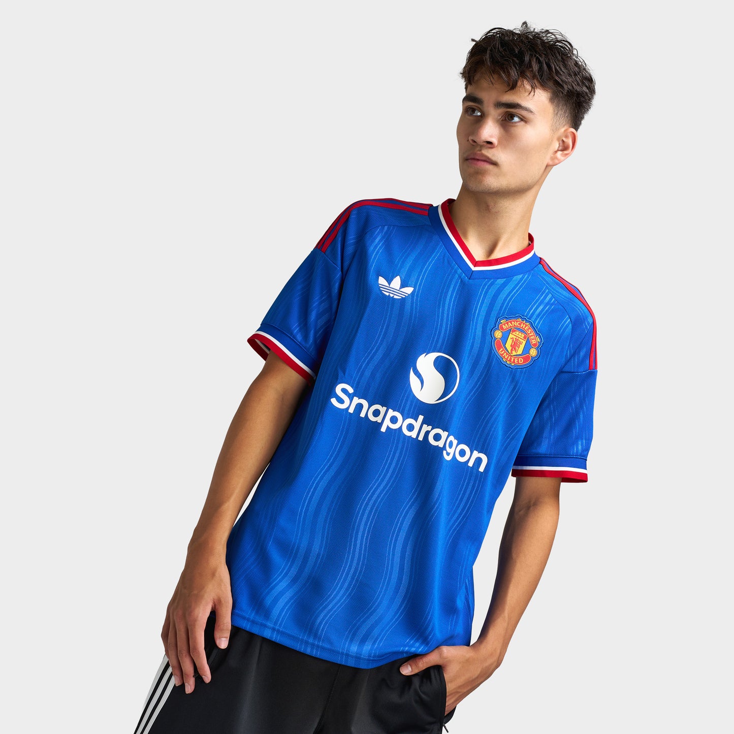 adidas Manchester United Away Jersey. Three-quarter view of model wearing team royal blue soccer jersey with red trim, Manchester United crest and sponsor graphic.