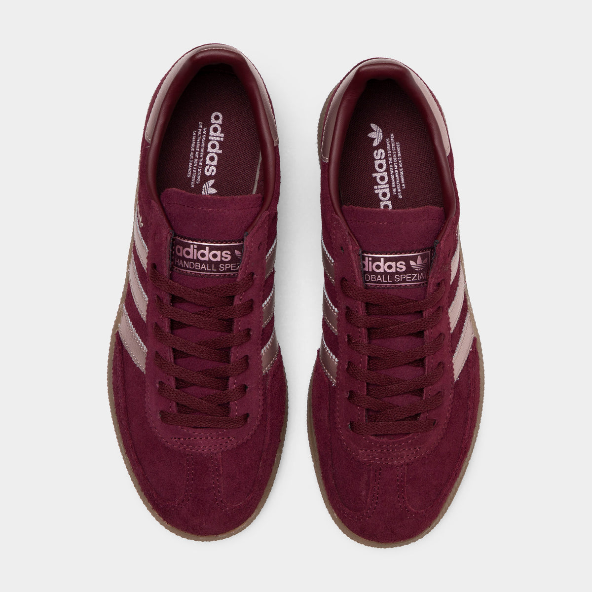 adidas Women's Handball Spezial. Top-down overhead view of a pair of low-top sneakers displaying maroon suede toe boxes with T-toe overlays, maroon laces, maroon tongues with vapour grey logo patches, and maroon insoles with adidas Trefoil branding. 