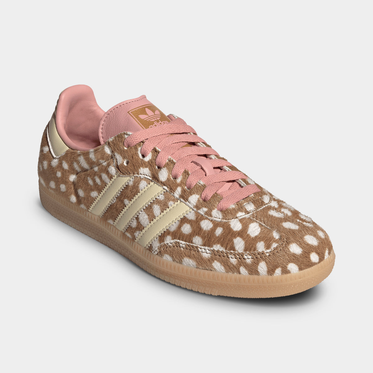 adidas Originals Women's Samba OG. Three-quarter view of single sneaker showcasing the brown desert and white spotted ponyhair upper, warm vanilla Three-Stripes, dusty pink laces, and gum rubber sole. 