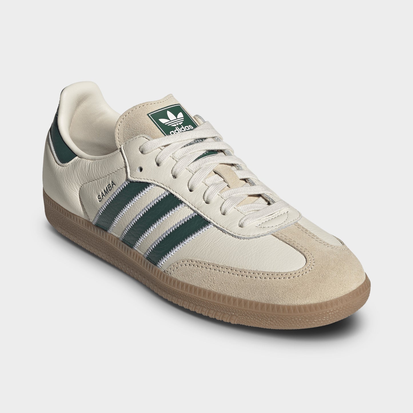 adidas Samba OG. Three-quarter view of cream, collegiate green and gum sneakers with cream laces, green stripes and gum soles.