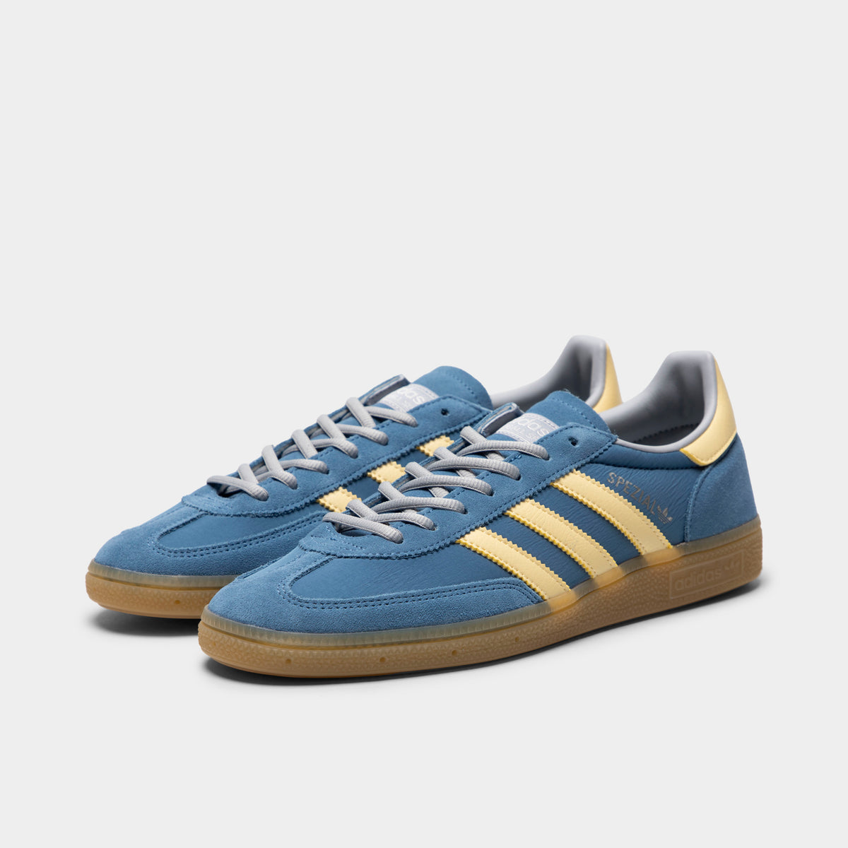 adidas Handball Spezial. Three-quarter view of dusky ink, easy yellow and gum sneakers with blue laces, yellow stripes and gum soles.