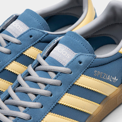 adidas Handball Spezial. Close-up of dusky ink, easy yellow and gum sneaker showing blue laces, yellow three stripes and gold Spezial branding.