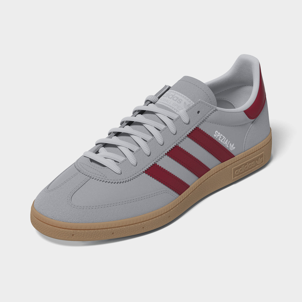 adidas Handball Spezial. Three-quarter view of halo silver, team victory red and gum sneakers with grey laces, red stripes and gum soles.