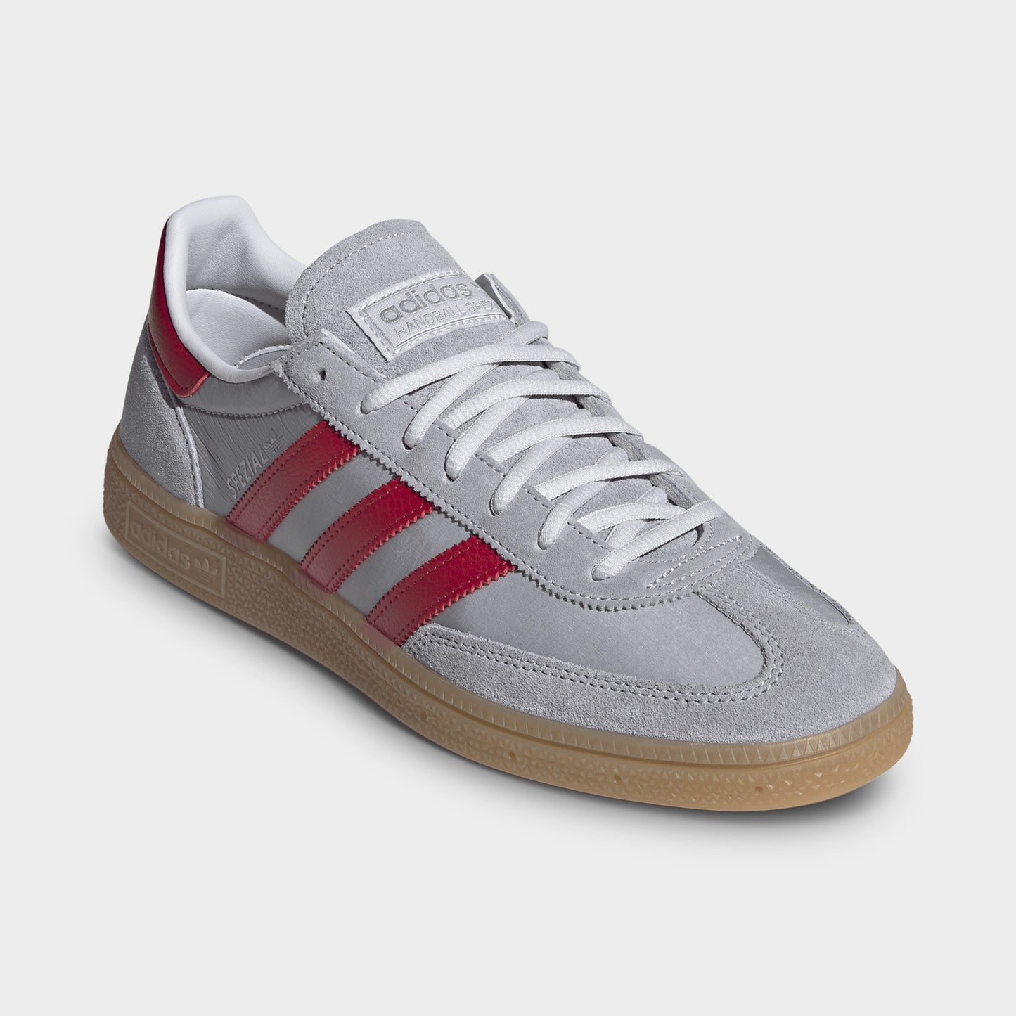 adidas Handball Spezial. Three-quarter view of halo silver, team victory red and gum sneaker with grey laces, red stripes and gum sole.