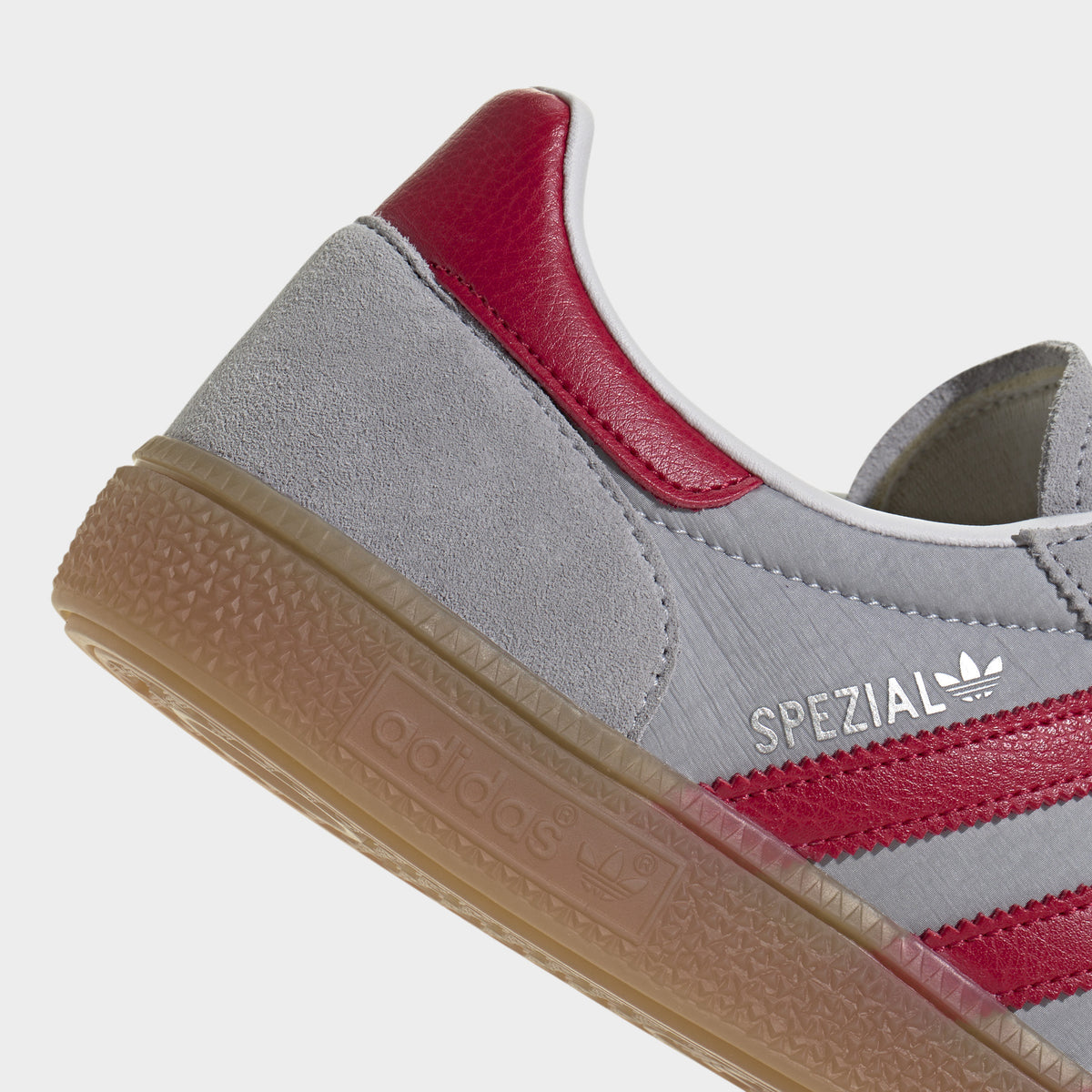 adidas Handball Spezial. Close-up of halo silver, team victory red and gum sneaker showing red heel tab, padded collar and textured gum sole edge.