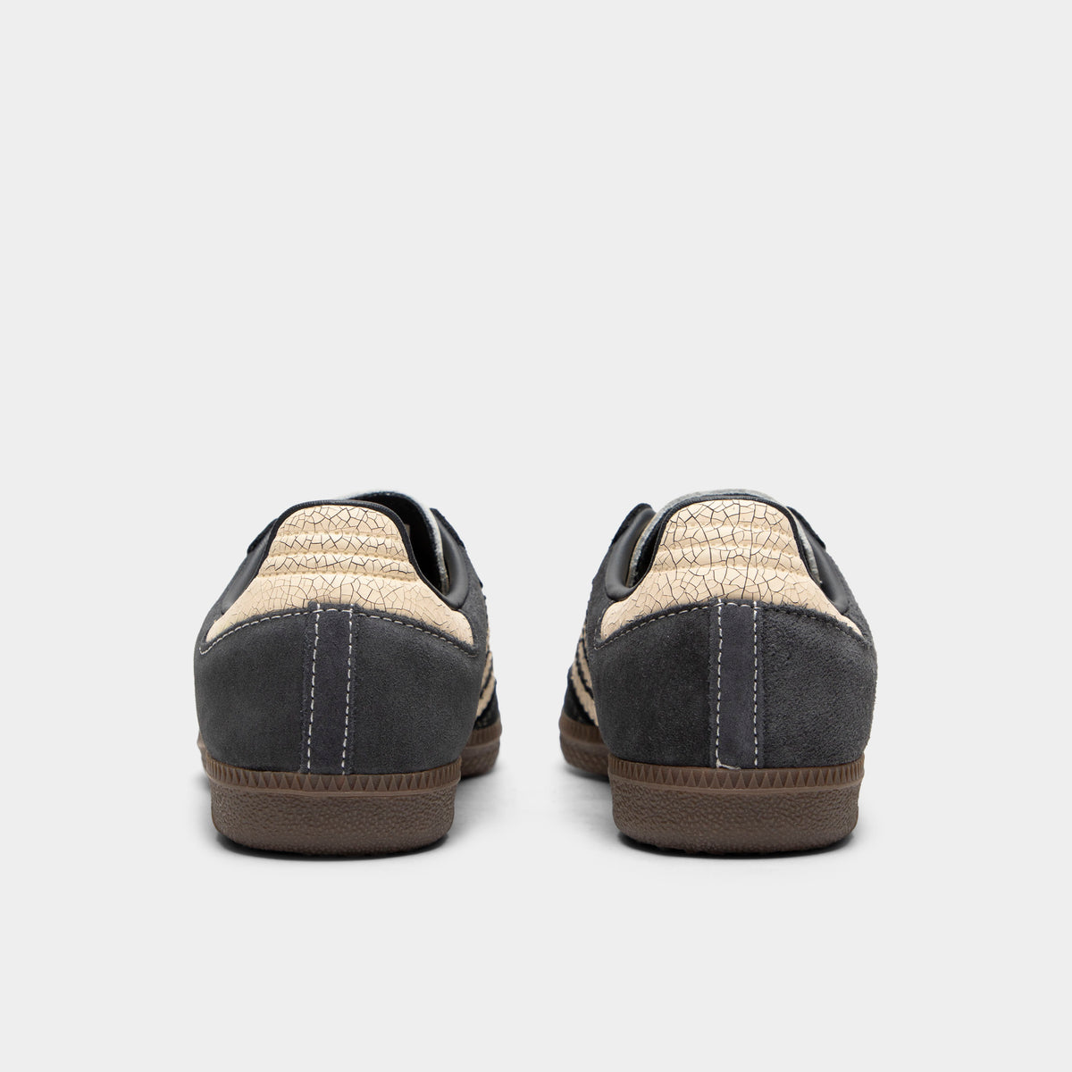 adidas Juniors' Samba OG. Rear view of a pair of low-top sneakers displaying carbon dark grey leather heel counters with stitching details, warm vanilla cracked leather heel tabs, and low-profile gum rubber soles. 