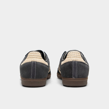 adidas Juniors' Samba OG. Rear view of a pair of low-top sneakers displaying carbon dark grey leather heel counters with stitching details, warm vanilla cracked leather heel tabs, and low-profile gum rubber soles. 