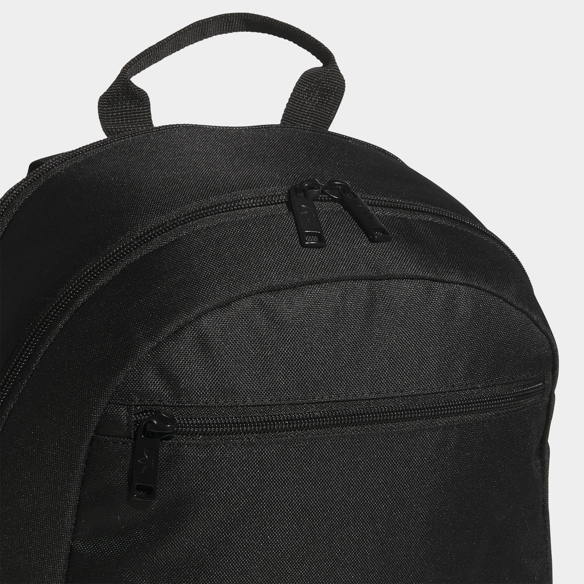 adidas Premise 2.0 Backpack. Close-up of black backpack showing top carry handle, upper zip compartment and stitched panel construction.