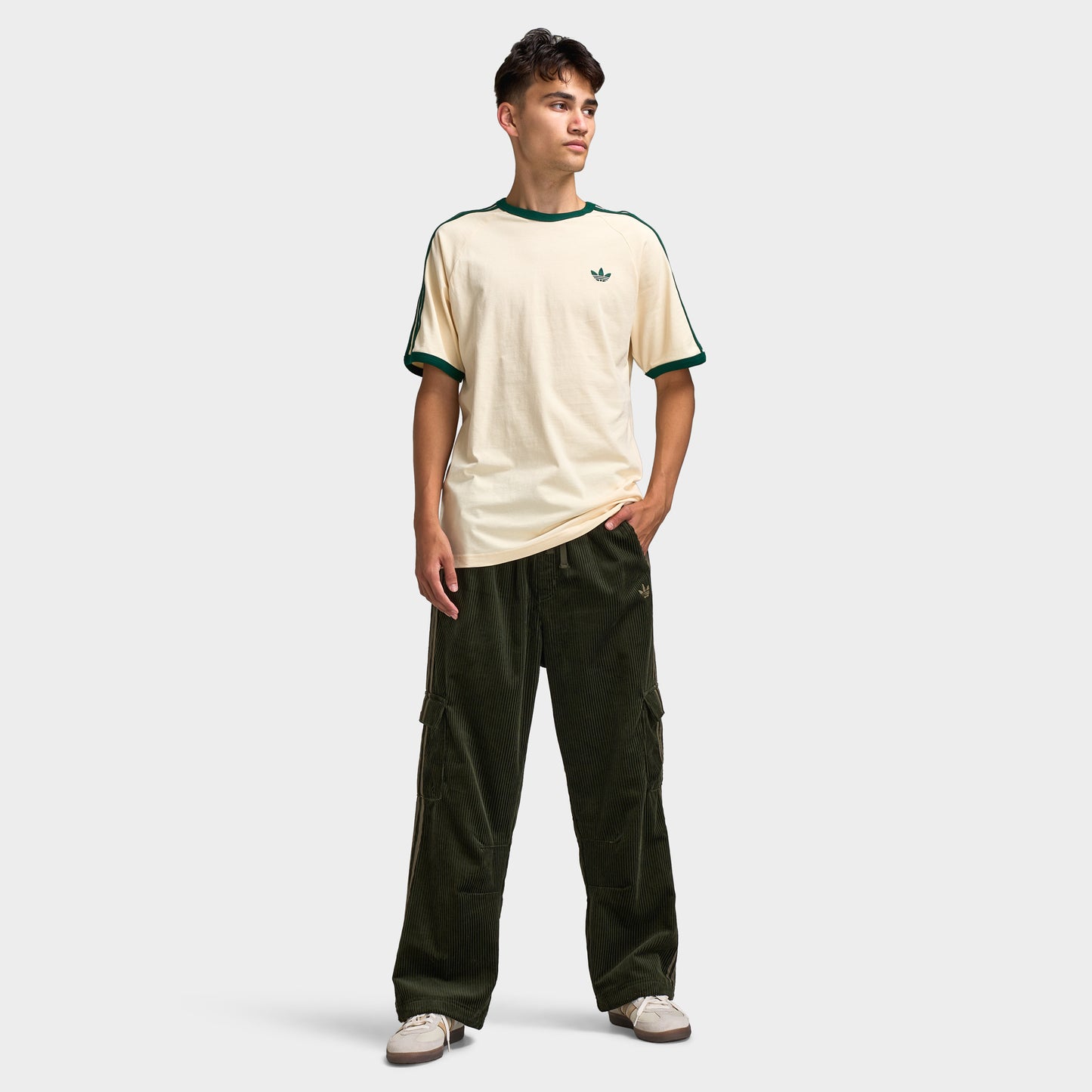adidas Adicolor Cord Cargo Pants. Full-body view of model wearing night cargo corduroy pants with a vanilla T-shirt and light-coloured shoes.