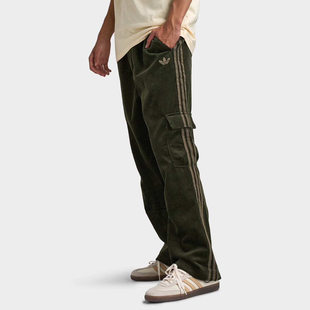 adidas Adicolor Cord Cargo Pants. Side view of model wearing night cargo corduroy pants with relaxed legs, cargo pockets and ribbed texture.