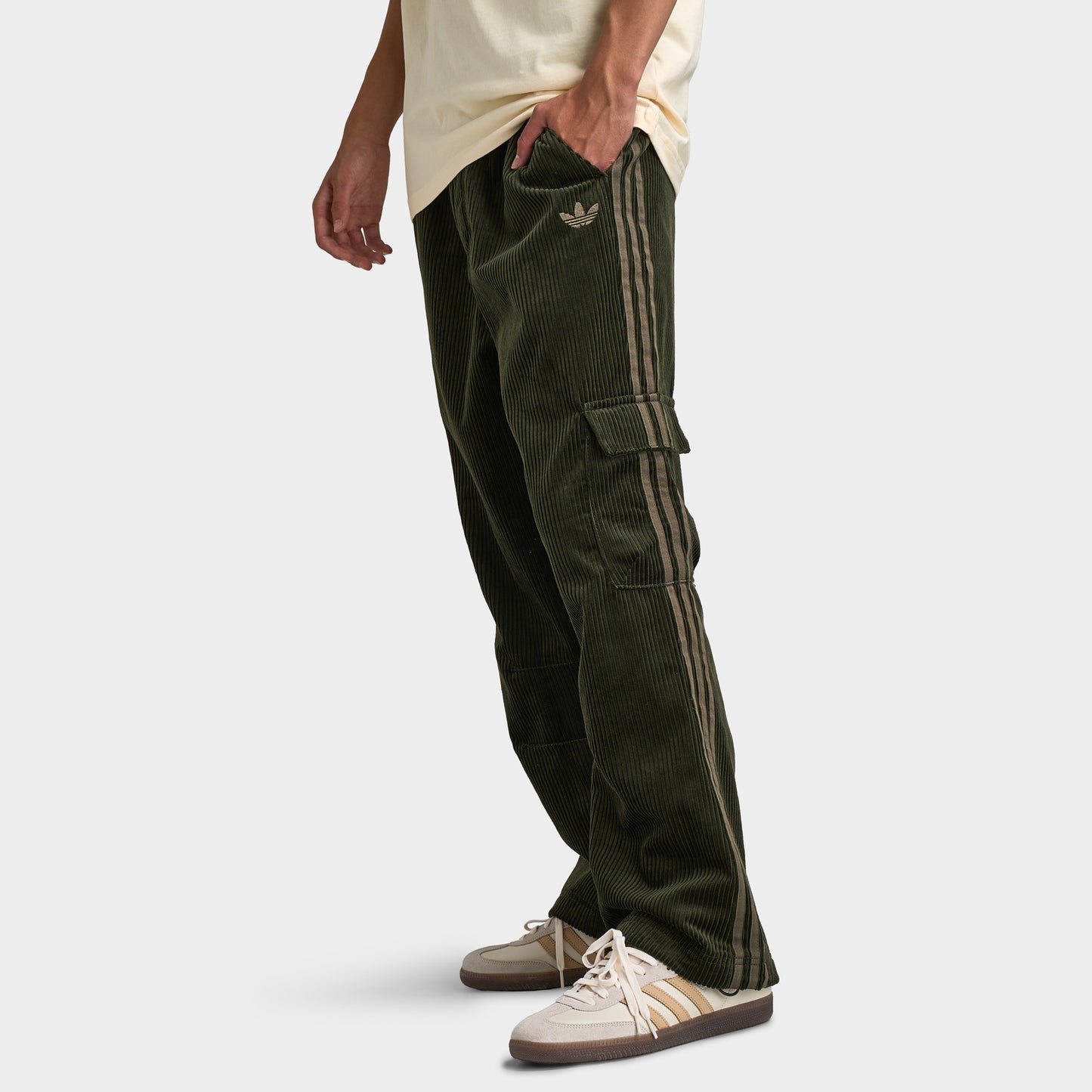 adidas Adicolor Cord Cargo Pants. Side view of model wearing night cargo corduroy pants with relaxed legs, cargo pockets and ribbed texture.