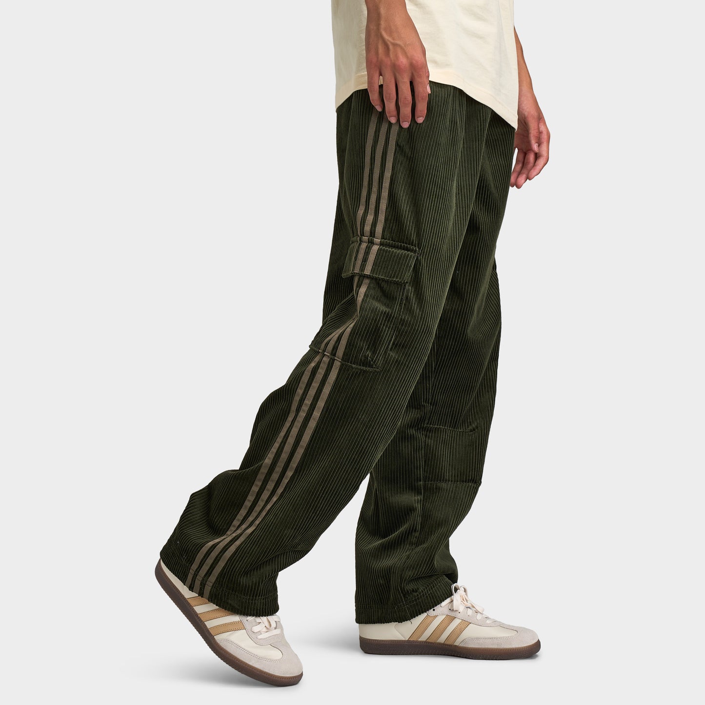 adidas Adicolor Cord Cargo Pants. Three-quarter view of model wearing night cargo corduroy pants with wide legs, side pockets and loose fit.