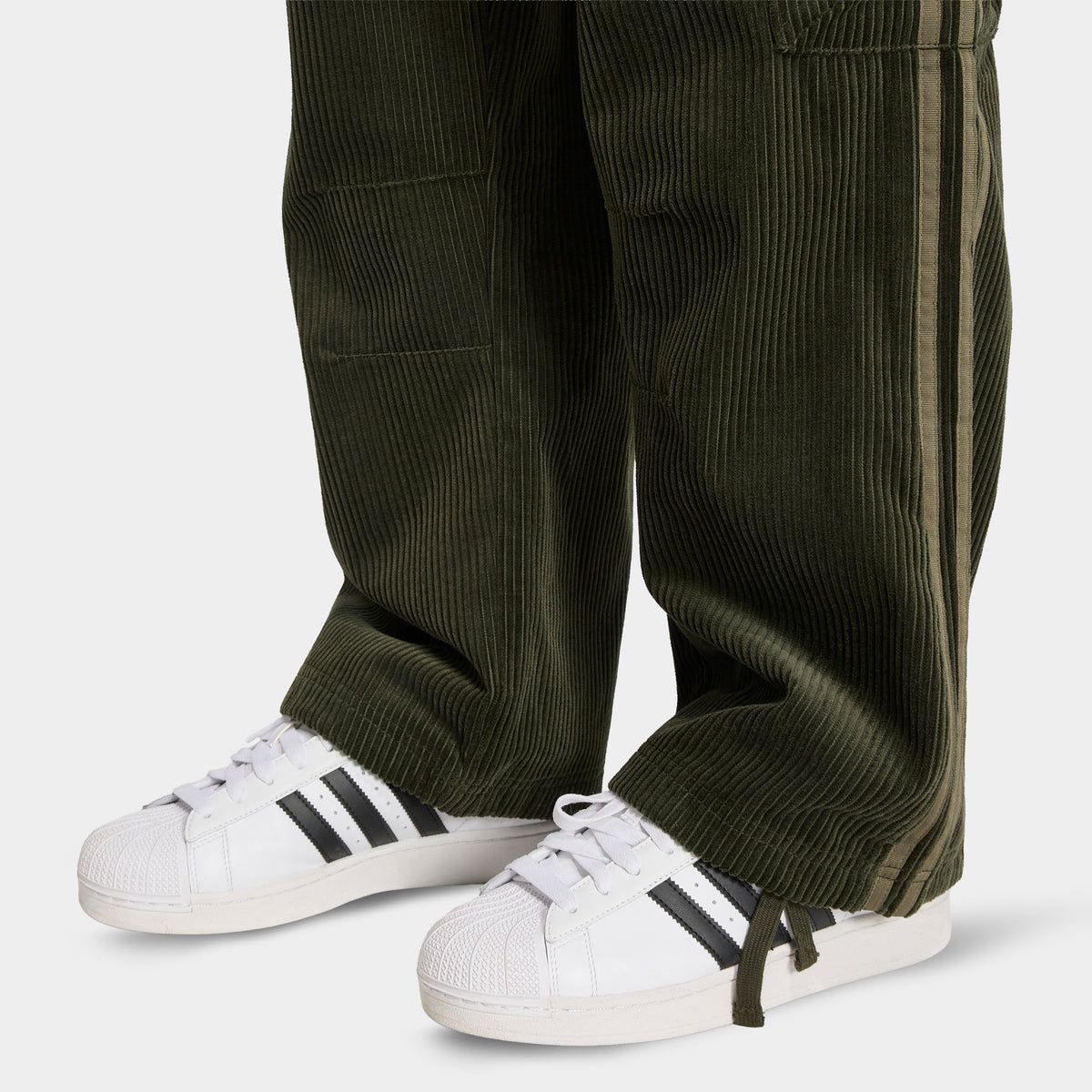 adidas Adicolor Cord Cargo Pants. Close-up of night cargo corduroy pants showing wide hems, ribbed texture and side cargo pocket.