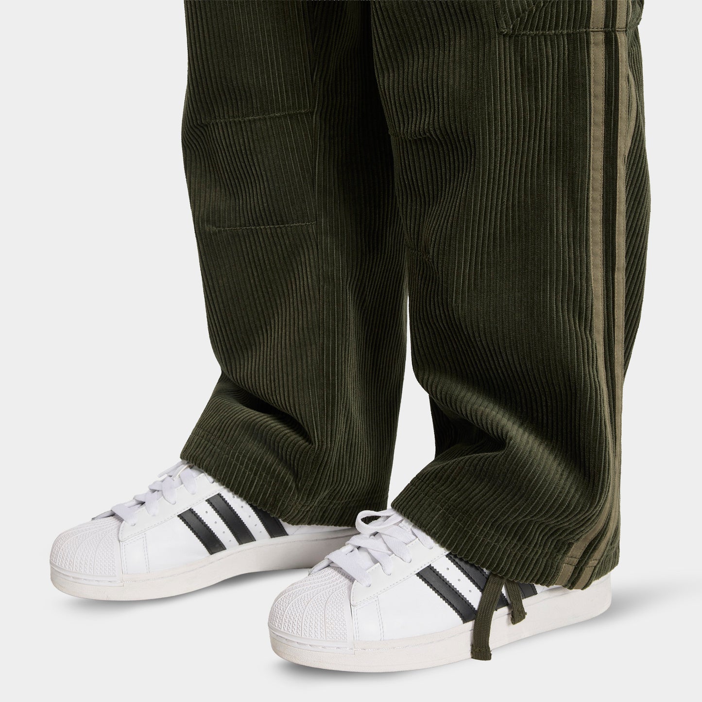 adidas Adicolor Cord Cargo Pants. Close-up of night cargo corduroy pants showing wide hems, ribbed texture and side cargo pocket.