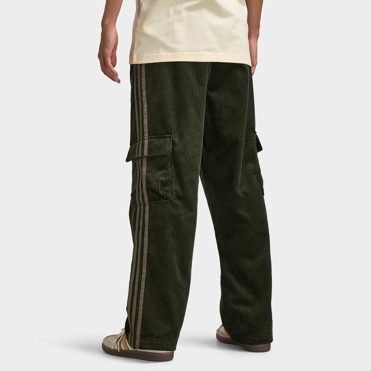 adidas Adicolor Cord Cargo Pants. Back view of model wearing night cargo corduroy pants with wide legs, rear pockets and relaxed silhouette.