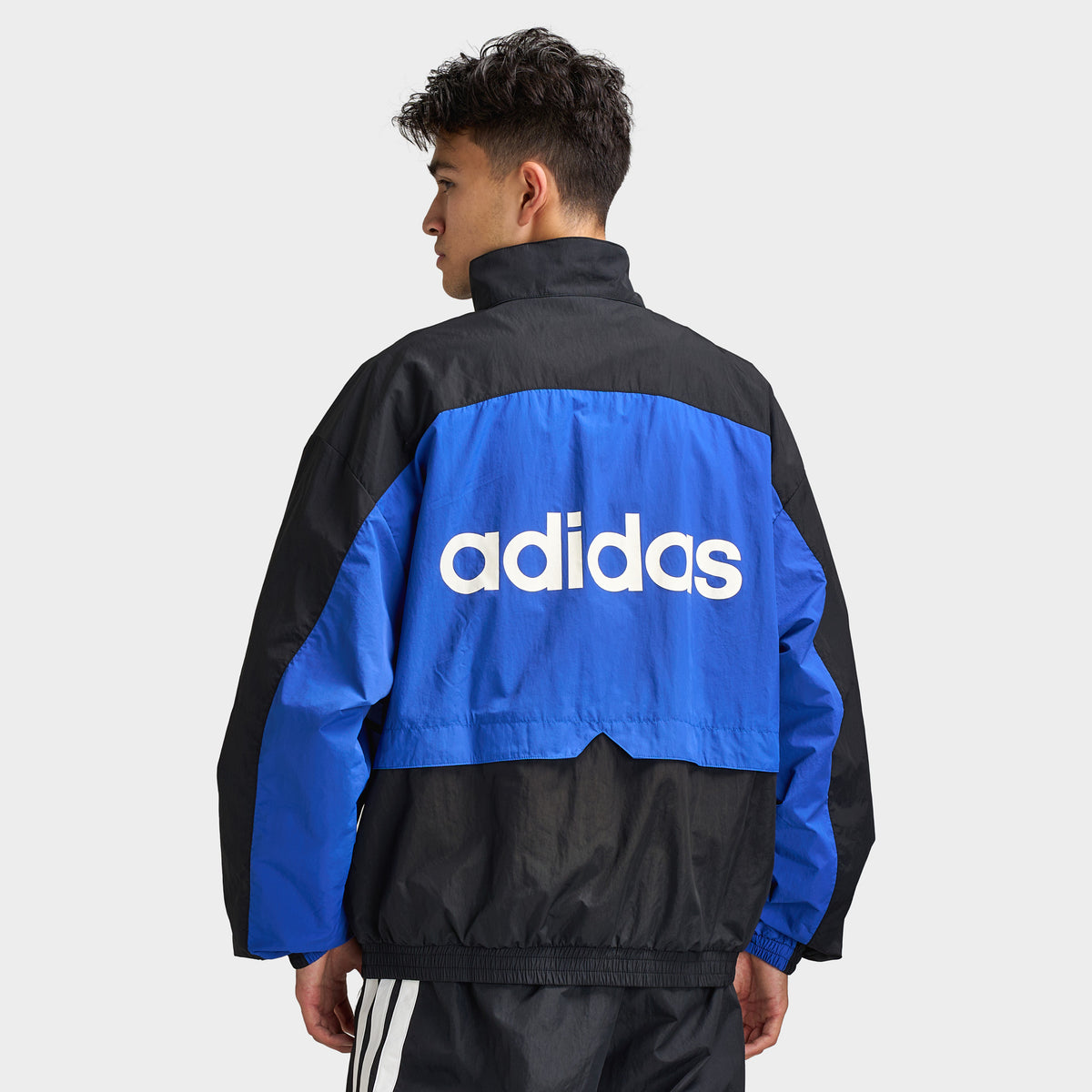 adidas Munich 93 Tracktop. Back view of model wearing blue and black track jacket with large white adidas logo across the upper back.