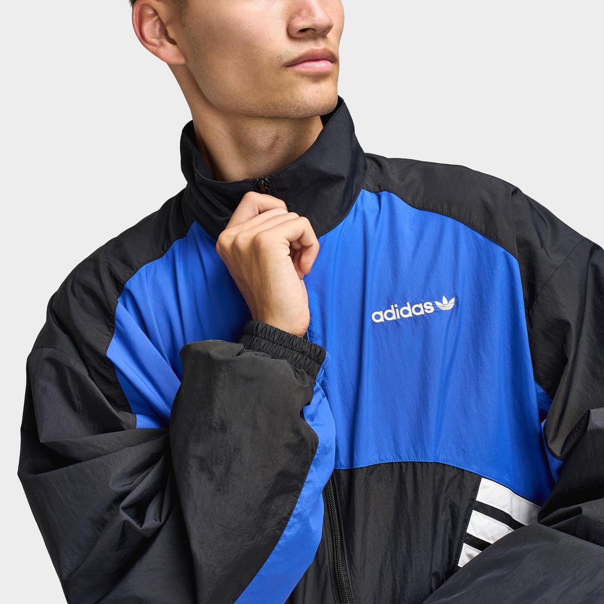 adidas Munich 93 Tracktop. Close-up of blue and black track jacket showing high collar, full-zip closure and contrast panel construction.
