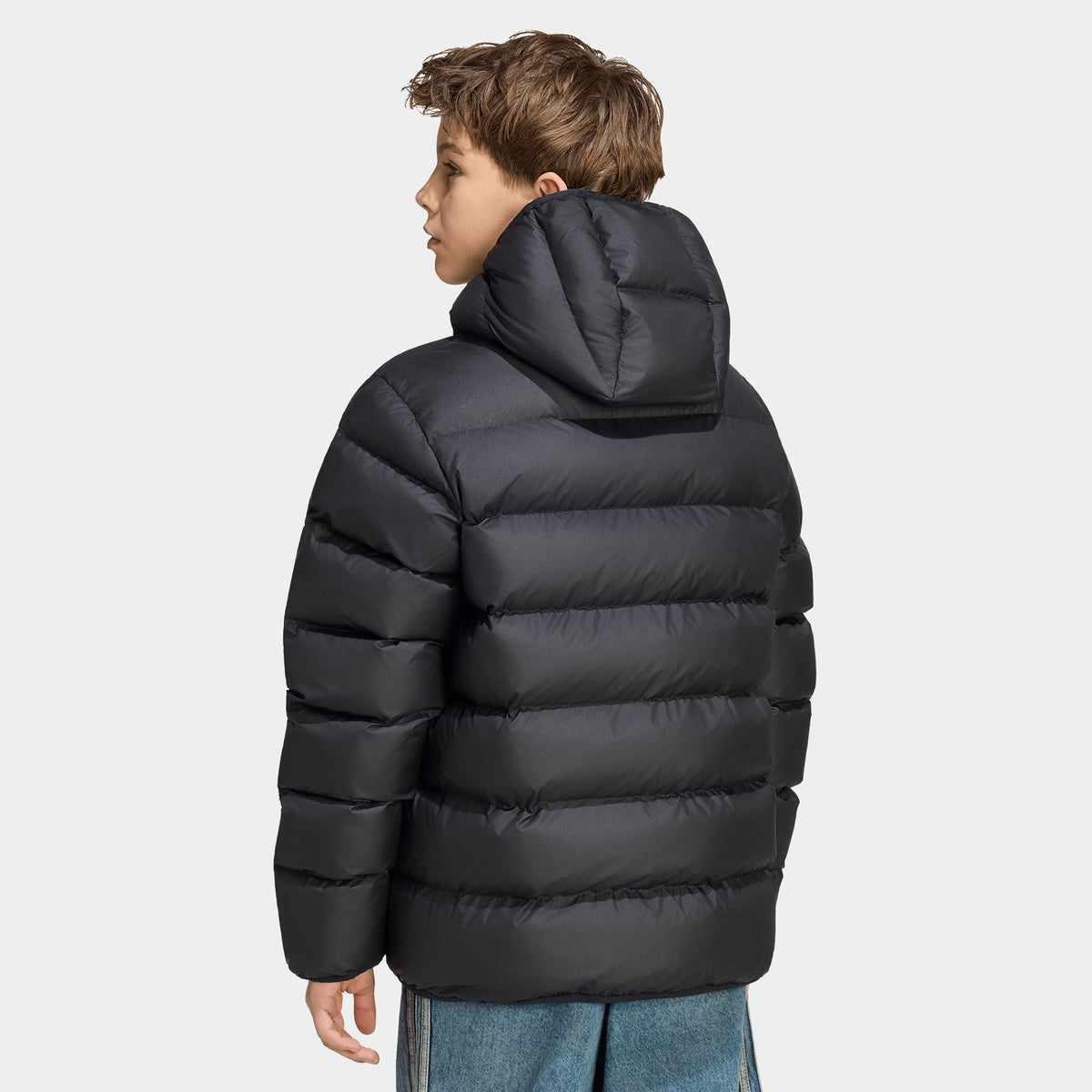 adidas Juniors' Blocking Regular Puffer. Upper body rear view showing the black hooded puffer jacket with continuous horizontal baffle quilting across the back and sleeves. 