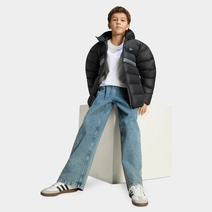 adidas Juniors' Blocking Regular Puffer. Full-length view of a youth model wearing the open black hooded puffer jacket paired with light wash denim jeans and white sneakers. 