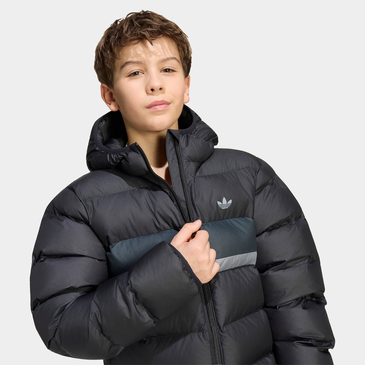 adidas Juniors' Blocking Regular Puffer. Medium close-up front view highlighting the full-zip closure, raised collar neck, horizontal quilting, grey chest stripe, and white adidas Trefoil logo. 