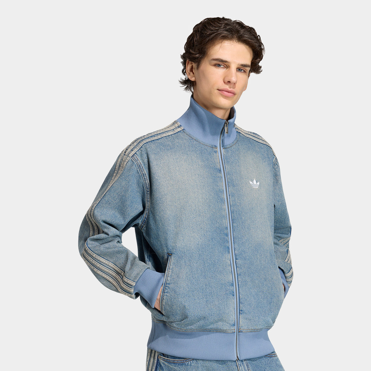 adidas Firebird Adicolor Track Top. Front view of model wearing worn blue denim track jacket with full-zip closure, high collar and white Trefoil chest logo.
