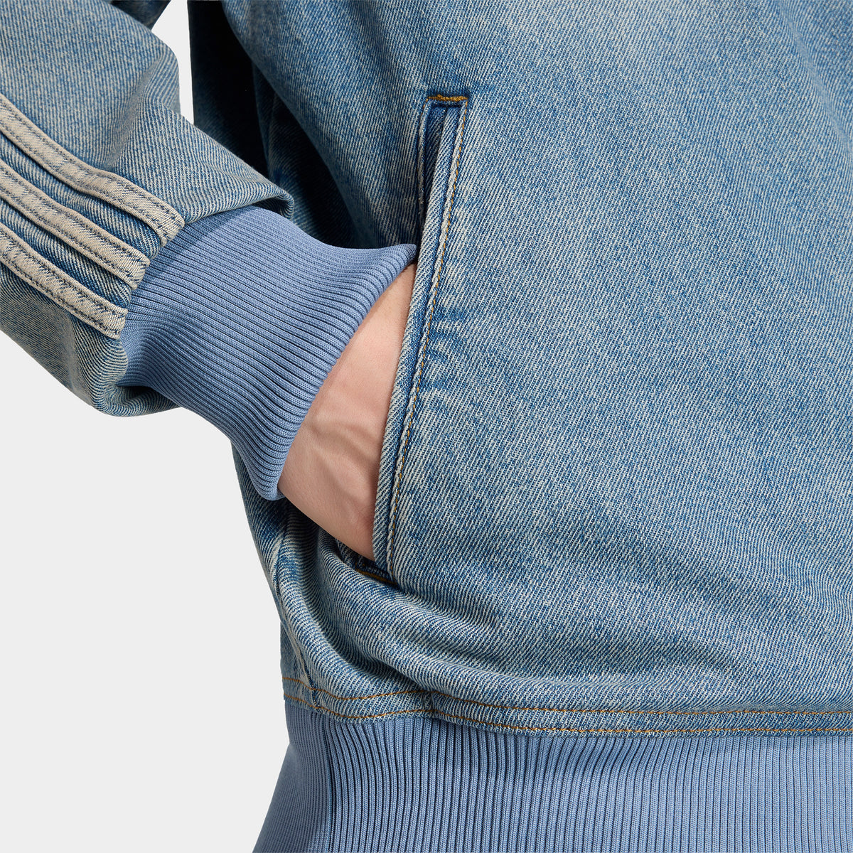 adidas Firebird Adicolor Track Top. Close-up of worn blue denim track jacket showing side pocket, contrast stitching and striped sleeve.