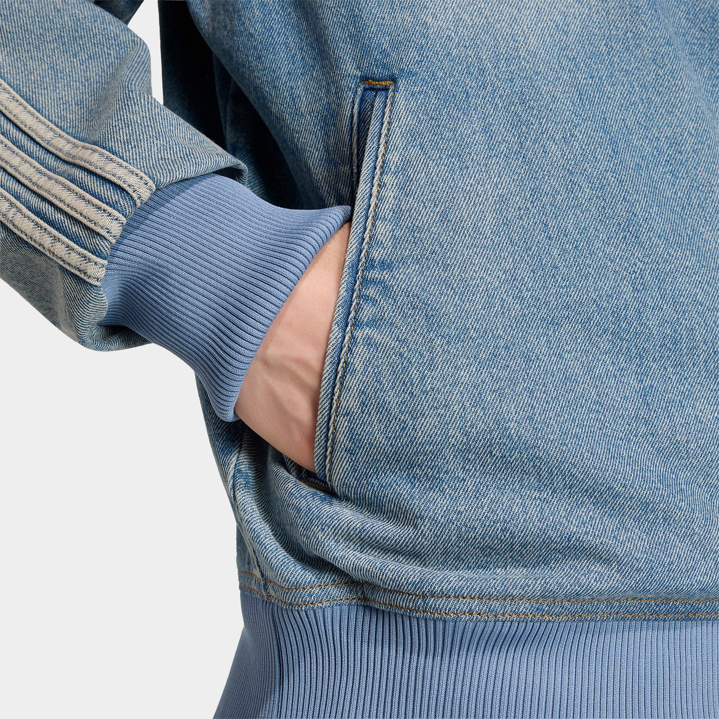adidas Firebird Adicolor Track Top. Close-up of worn blue denim track jacket showing side pocket, contrast stitching and striped sleeve.