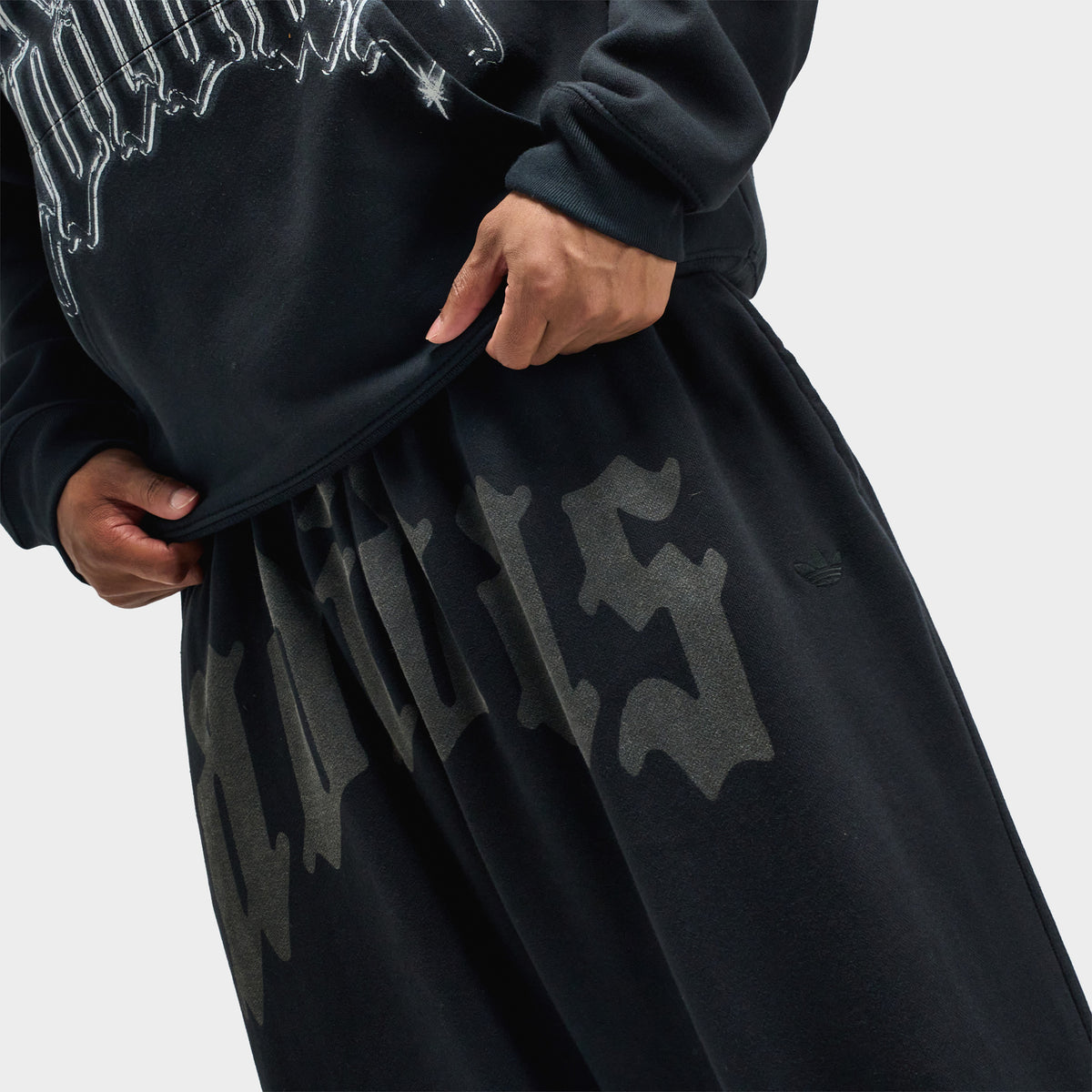 adidas Wide Leg Sweatpants. Close-up view showcasing the elastic waistband and oversized dark grey gothic "adidas" text print across the upper thighs. 