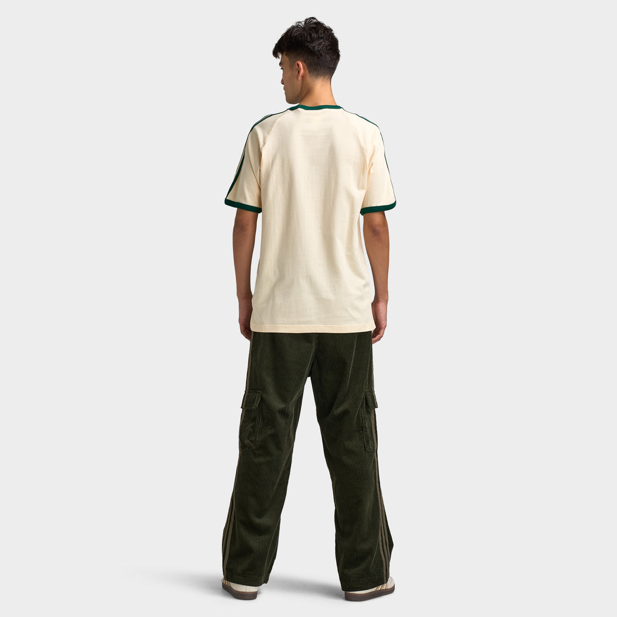 adidas 3 Stripes T-Shirt. Full-body back view of model wearing vanilla and collegiate green T-shirt with dark green pants and light-coloured shoes.