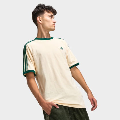 adidas 3 Stripes T-Shirt. Three-quarter view of model wearing vanilla and collegiate green T-shirt with striped sleeves, green collar trim and relaxed silhouette.