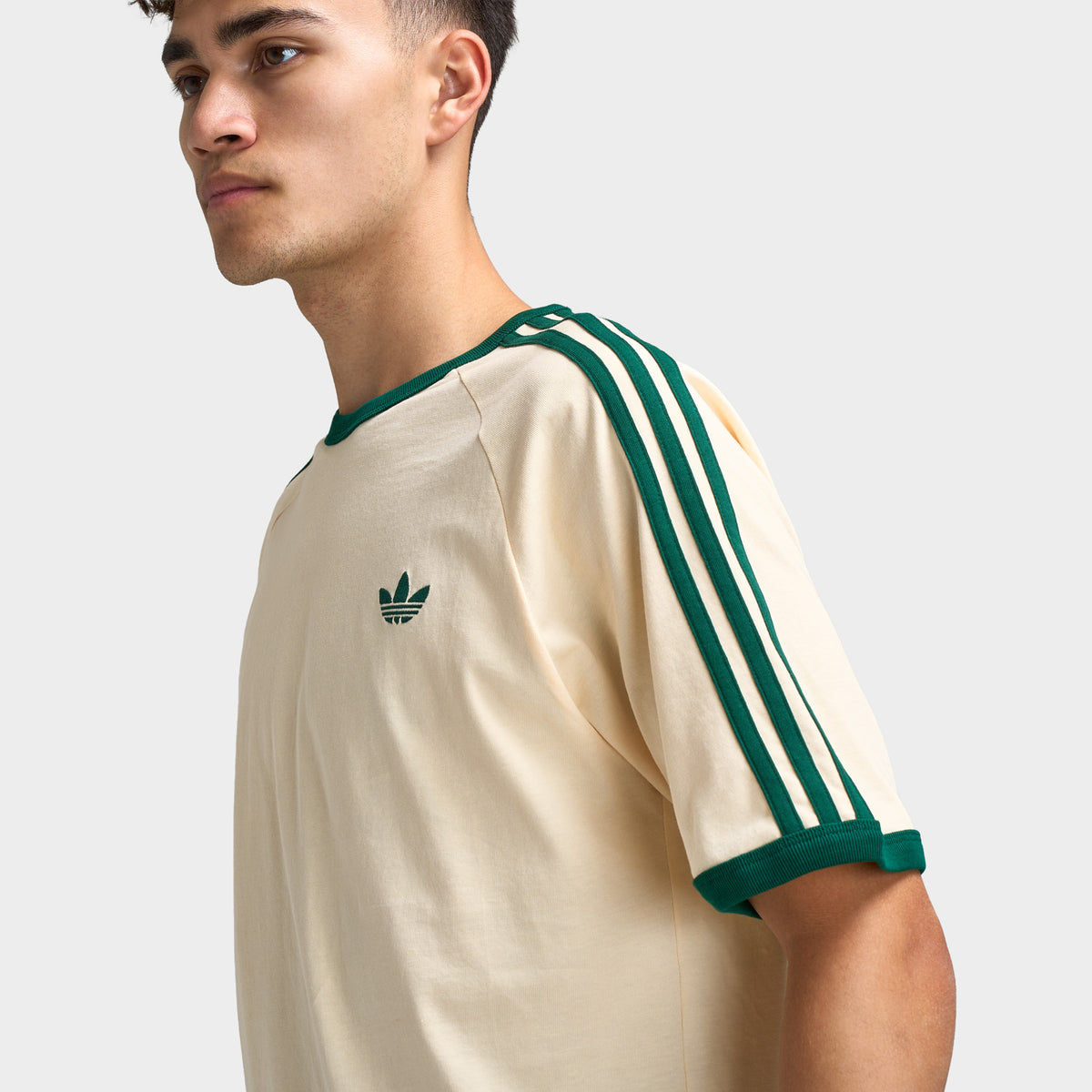 adidas 3 Stripes T-Shirt. Close-up of vanilla and collegiate green T-shirt showing green three stripes along the sleeve, contrast collar and Trefoil chest logo.