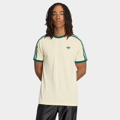 adidas 3 Stripes T-Shirt. Front view of model wearing vanilla and collegiate green T-shirt with green collar trim, sleeve stripes and Trefoil chest logo.