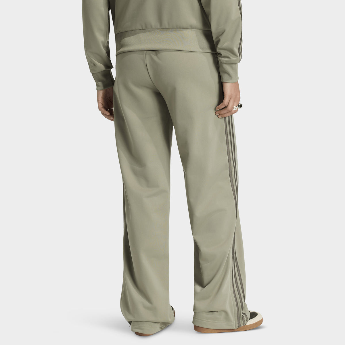 adidas Firebird Loose Track Pants. Back view of model wearing silver-pebble branch track pants with wide legs and tonal side stripes.