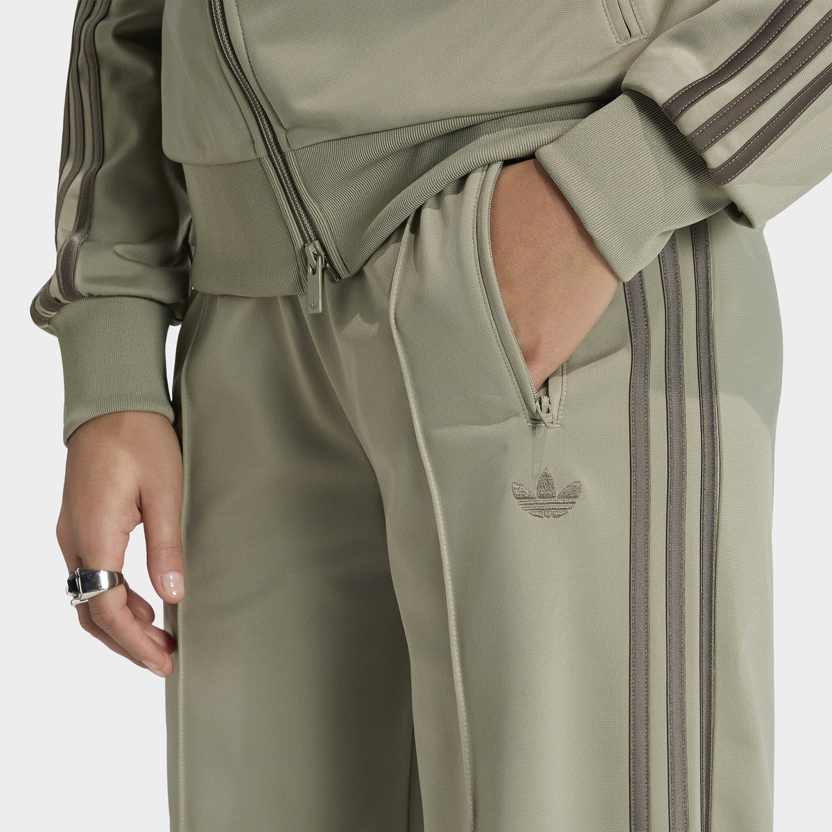 adidas Firebird Loose Track Pants. Close-up of silver-pebble branch track pants showing side pocket, elastic waistband and tonal three stripes.