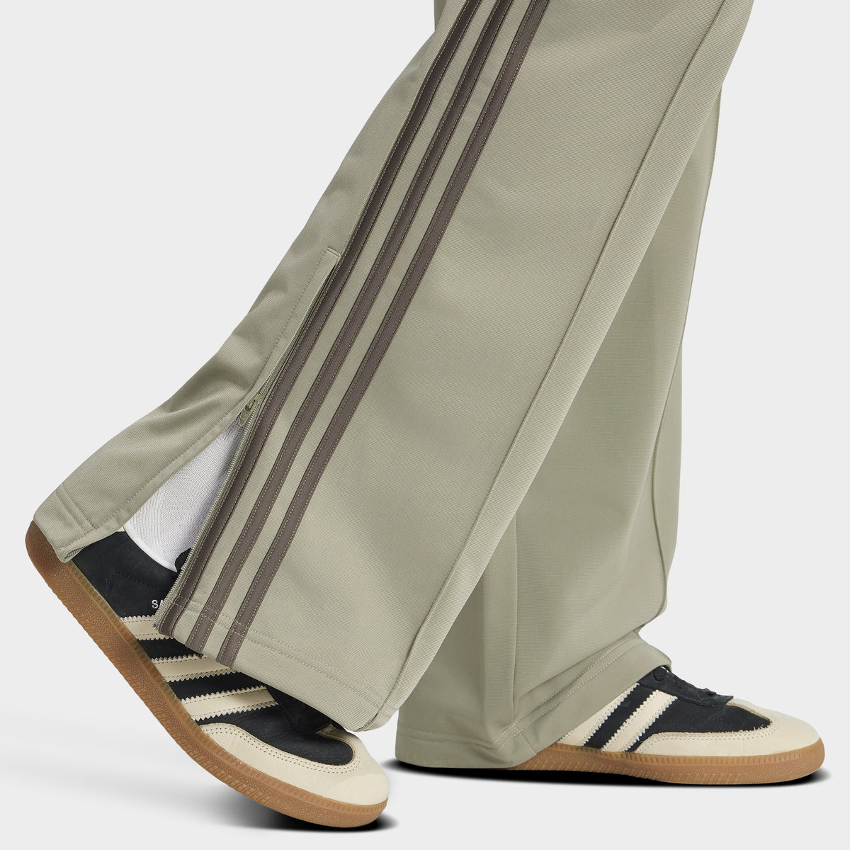 adidas Firebird Loose Track Pants. Close-up of silver-pebble branch track pants showing wide-leg hems and tonal side stripes over sneakers.