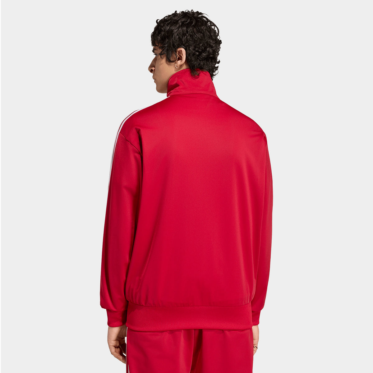 adidas Firebird Track Top. Back view of team victory red track jacket with white sleeve stripes, high collar and straight hem.