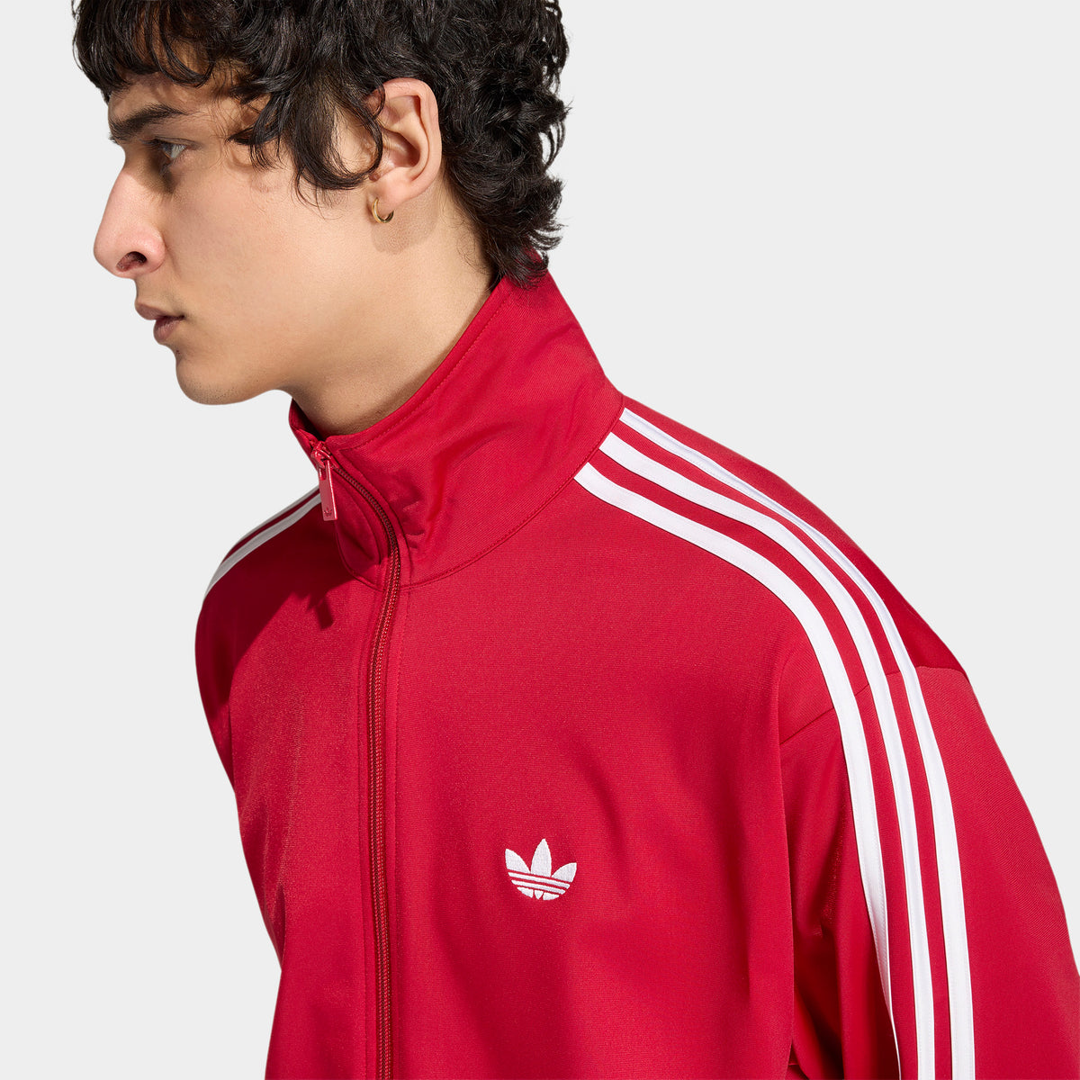 adidas Firebird Track Top. Close-up of team victory red track jacket showing high collar, full-zip closure, white stripes and Trefoil logo.