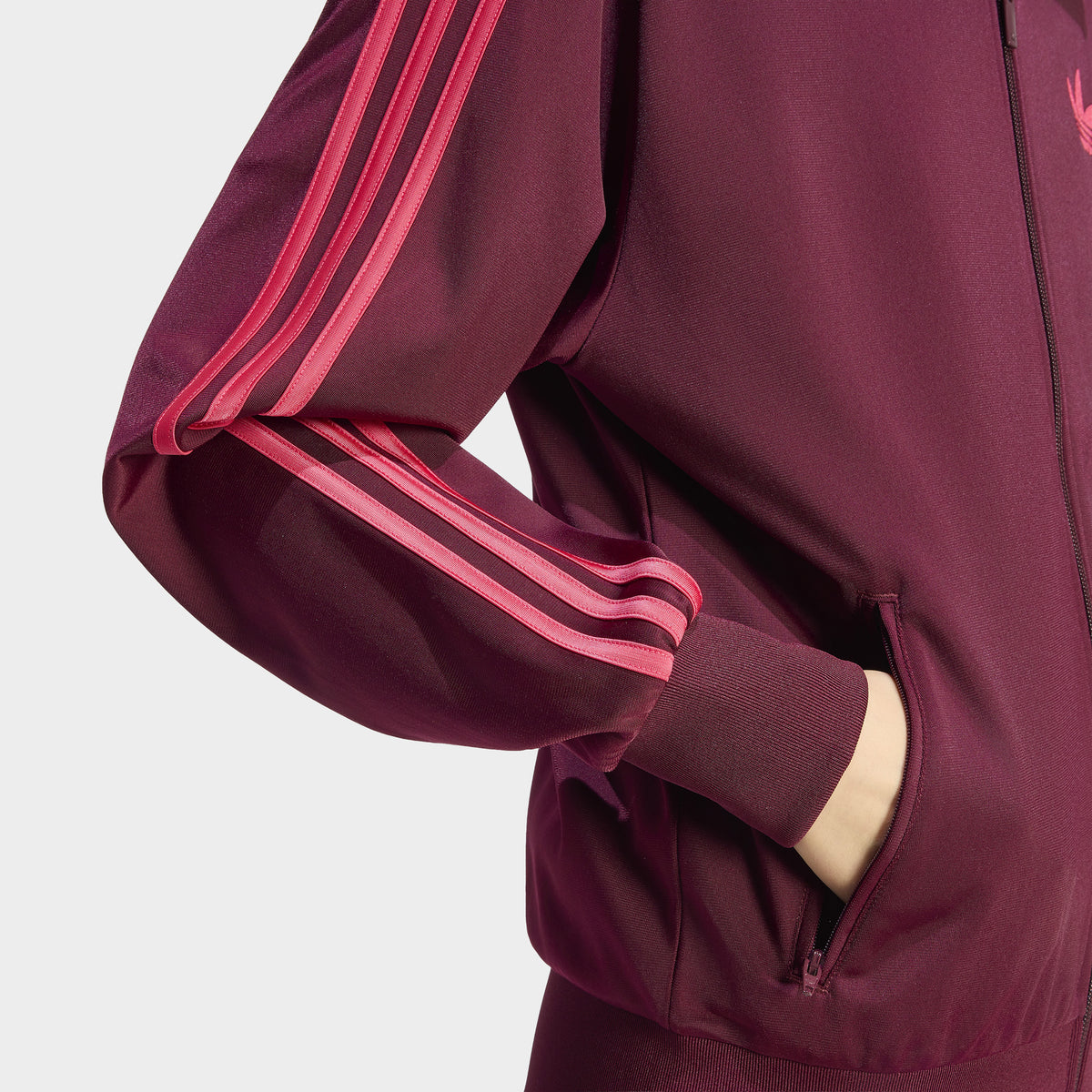 adidas Firebird Track Jacket Loose. Close-up of a maroon track jacket showing the power pink 3-Stripes down the sleeve and the side pocket.