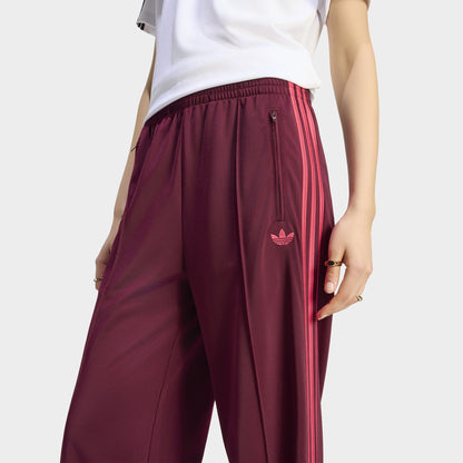 adidas Firebird Loose Track Pant. Close-up of maroon track pants showing the waistband, loose silhouette and embroidered Trefoil logo near the hip.