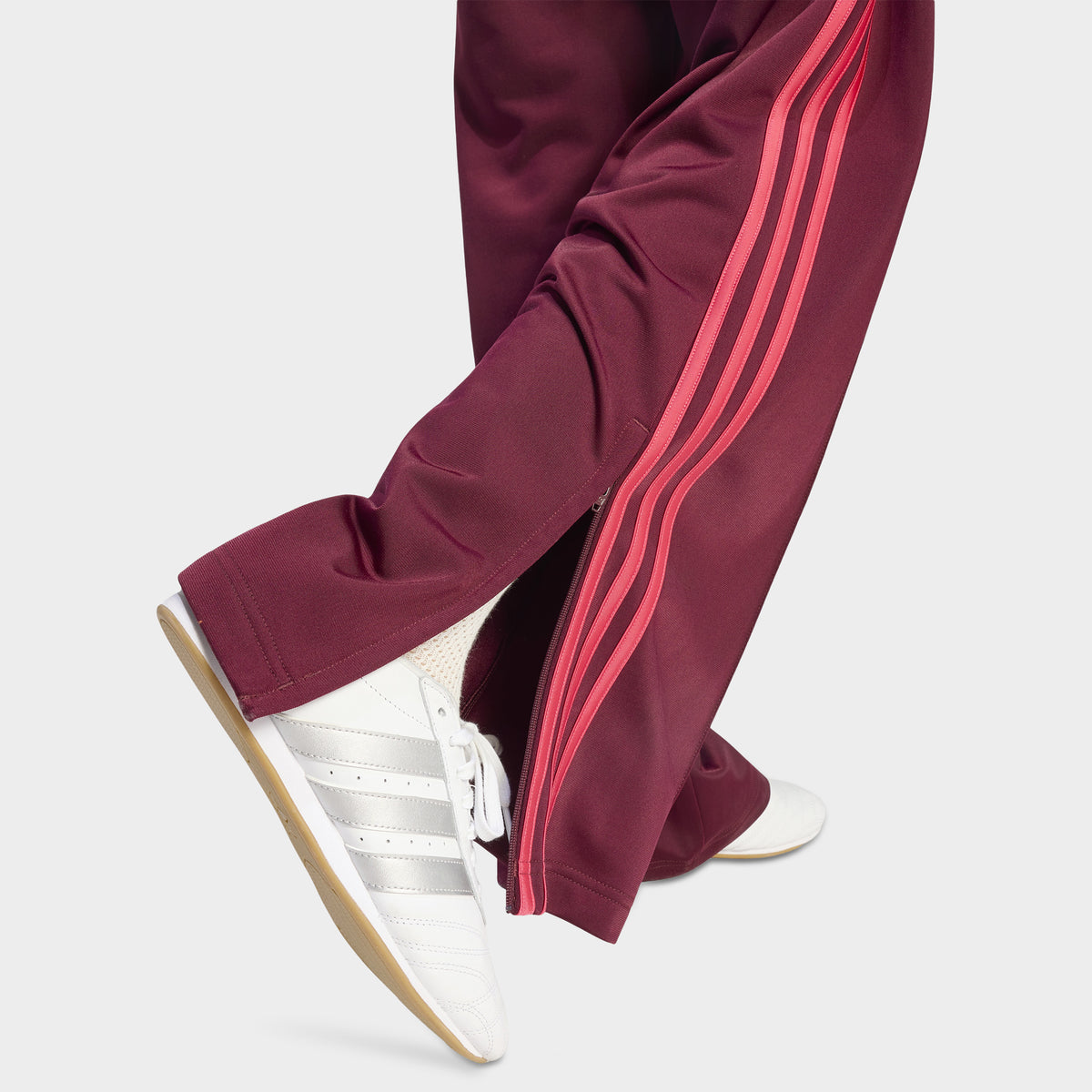 adidas Firebird Loose Track Pant. Close-up of maroon track pants showing the power pink side stripes and loose hem.