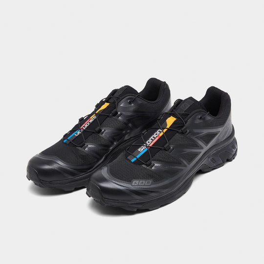 Salomon XT-6. Three-quarter view of black and phantom trail sneakers with quick-lace closure, layered uppers and multicolour tongue accents.