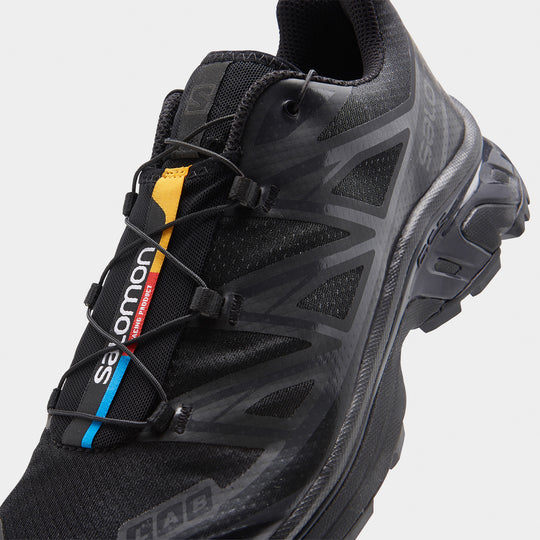Salomon XT-6. Close-up of black and phantom trail sneaker showing quick-lace closure, layered panels and multicolour tongue detail.