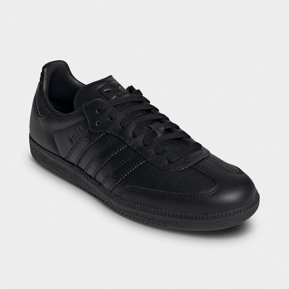 adidas Samba OG. Three-quarter view of black sneakers with black laces, tonal stripes and low-profile soles.