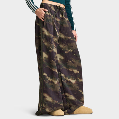 adidas Women's Camouflage Adilenium Track Pant. Side profile model view showing night cargo, aurora coffee, and olive strata camouflage track pants, side seam 3-Stripes detail, wide-leg cut, and open hem. 