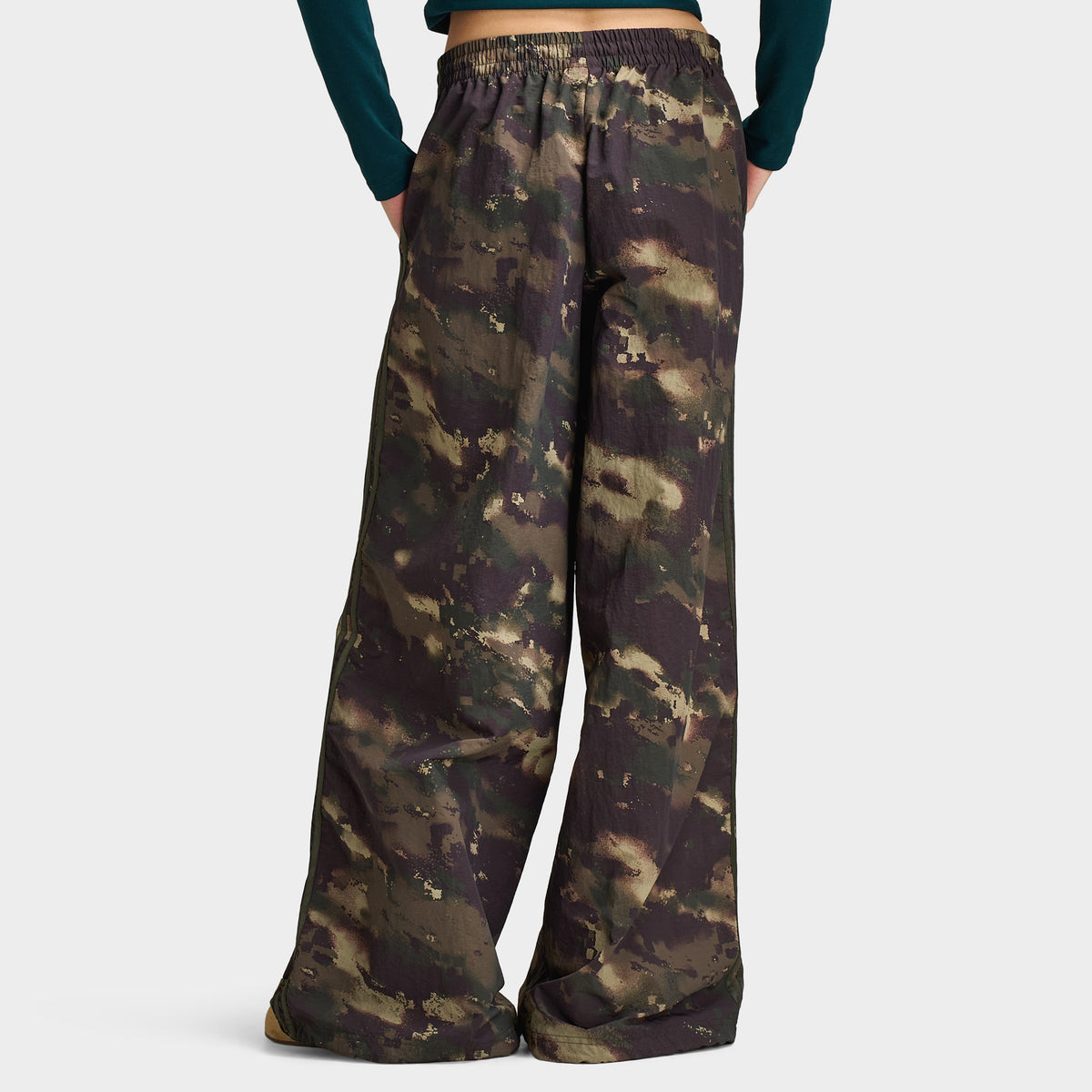 adidas Women's Camouflage Adilenium Track Pant. Lower body rear model view showing the back profile of night cargo, aurora coffee, and olive strata camouflage wide-leg track pants, elasticated waistband, relaxed loose fit, and open hems. 