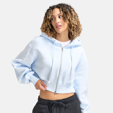Woman wears Nike Sportswear Women's Phoenix Fleece Loose Crop Full Zip Hoodie "Blue Tint / Sail". Shop Women's Clothing now.