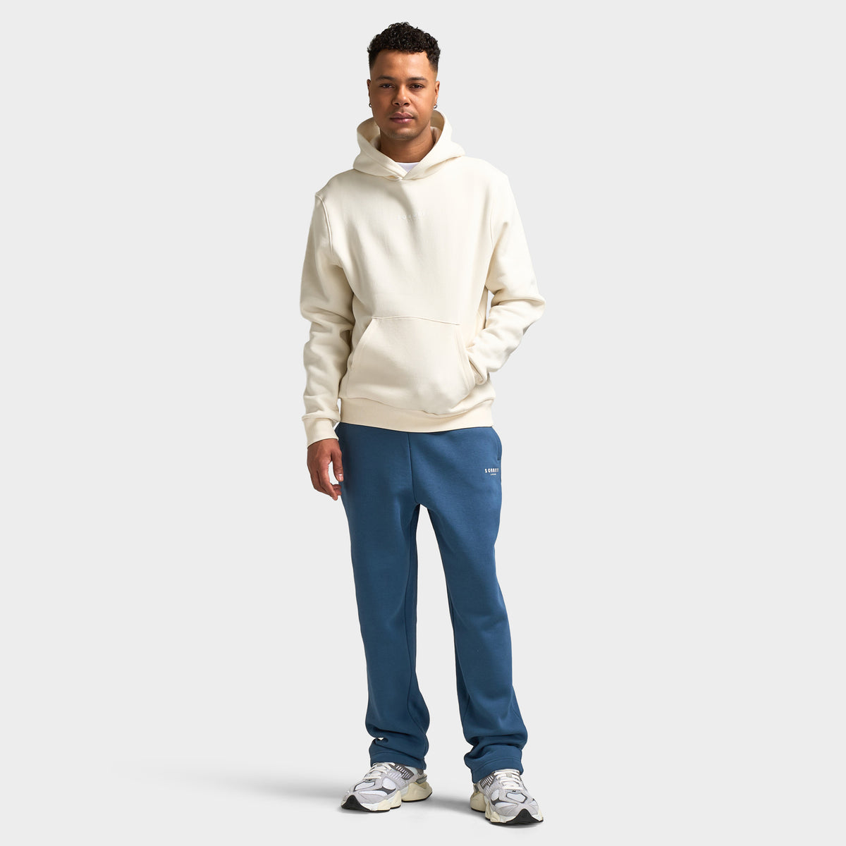 Sonneti London Hoodie 2.0. Full-body front view of model wearing egret hoodie with blue pants and white sneakers.