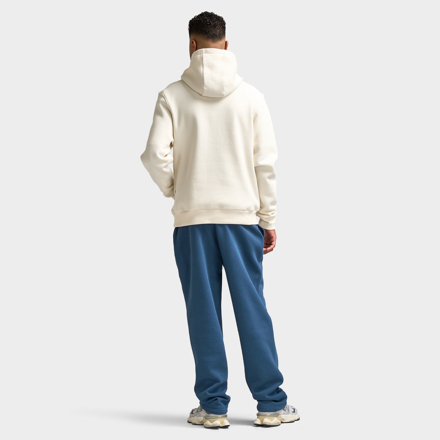 Sonneti London Hoodie 2.0. Full-body back view of model wearing egret hoodie with blue pants and white sneakers.