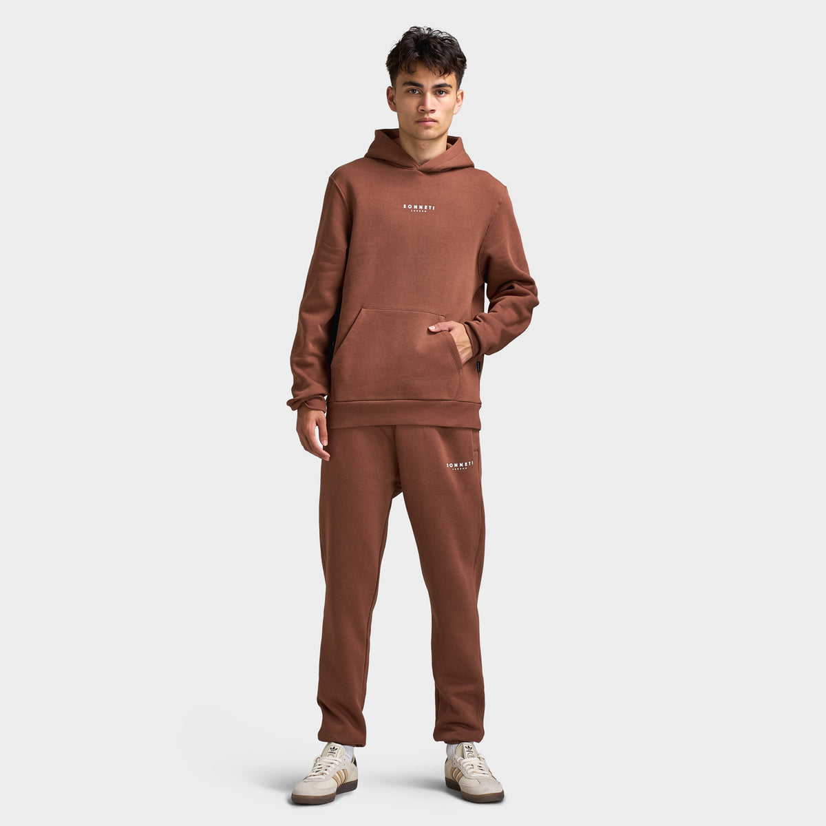Sonneti London Hoodie 2.0. Full-body front view of model wearing cocoa brown hoodie with matching pants and white sneakers.